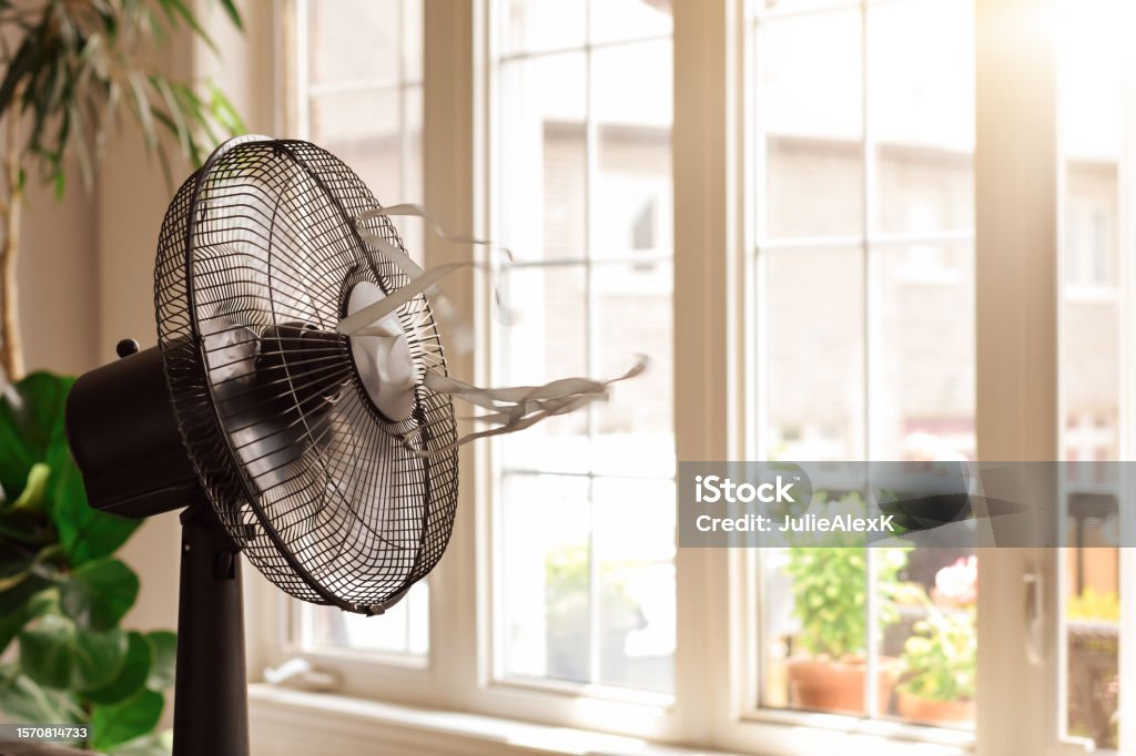 electric cooling fan with blowing ribbons in front of window on hot summer day